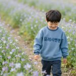 여름 키즈 반팔 아노락 스타일과 기능 디스커버리키즈 프레시벤트 반팔 아노락을 입고 유채꽃밭에서 웃고 있는 초등 남아